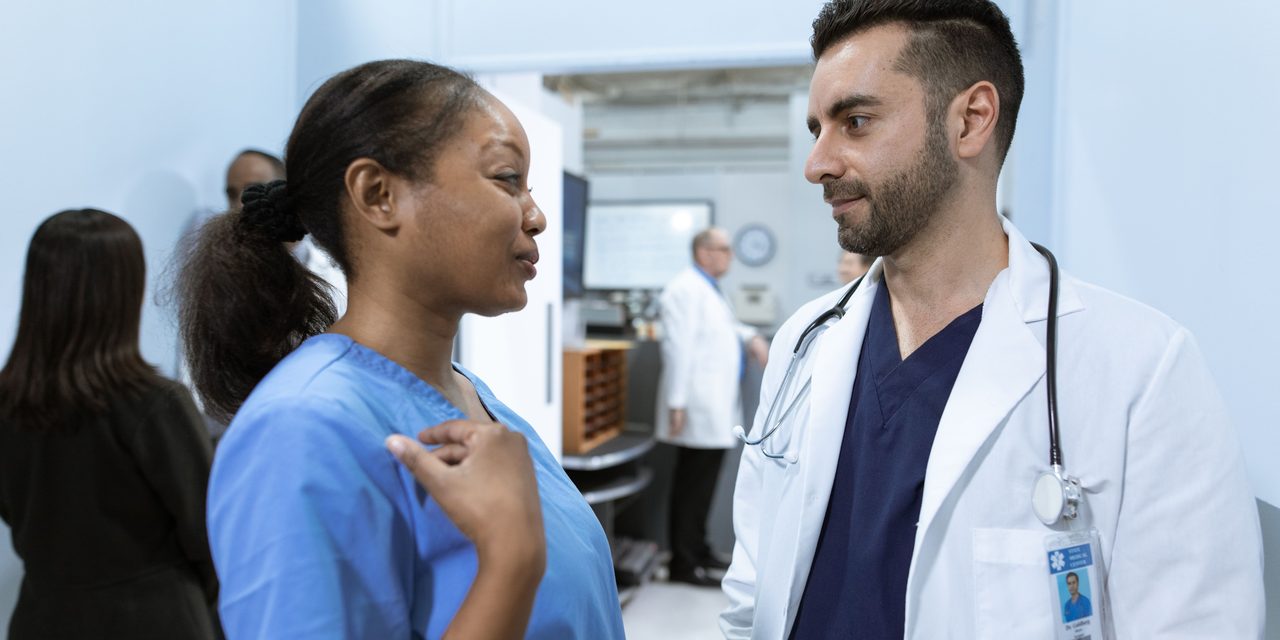 A physician and a member of clinical staff in conversation in a healthcare facility hallway